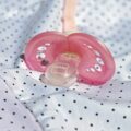 Pink baby pacifier lying on a white polka dot blanket